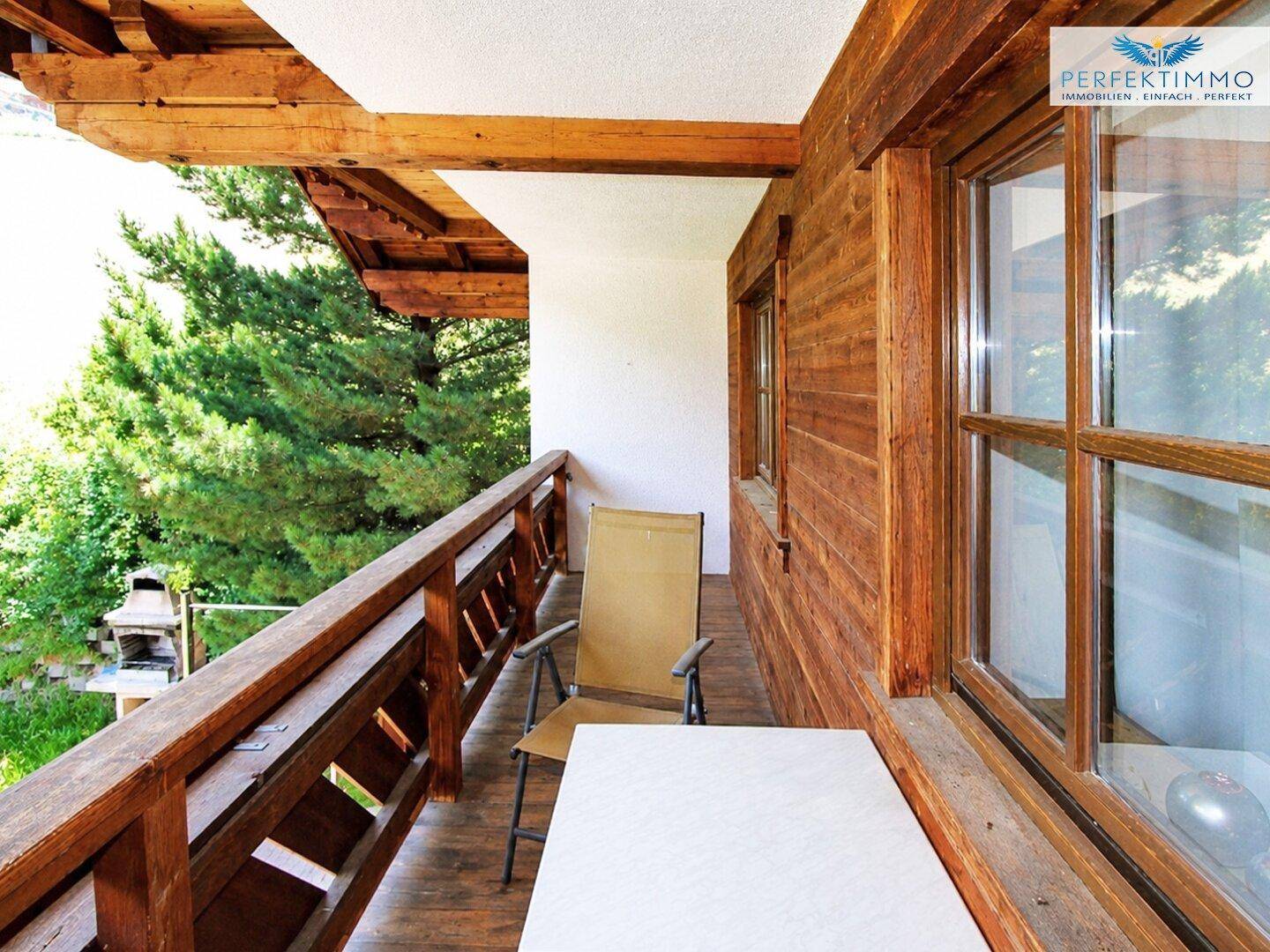 Rustikaler Holzbalkon mit Sitzgelegenheiten und Blick auf die grüne Berglandschaft.