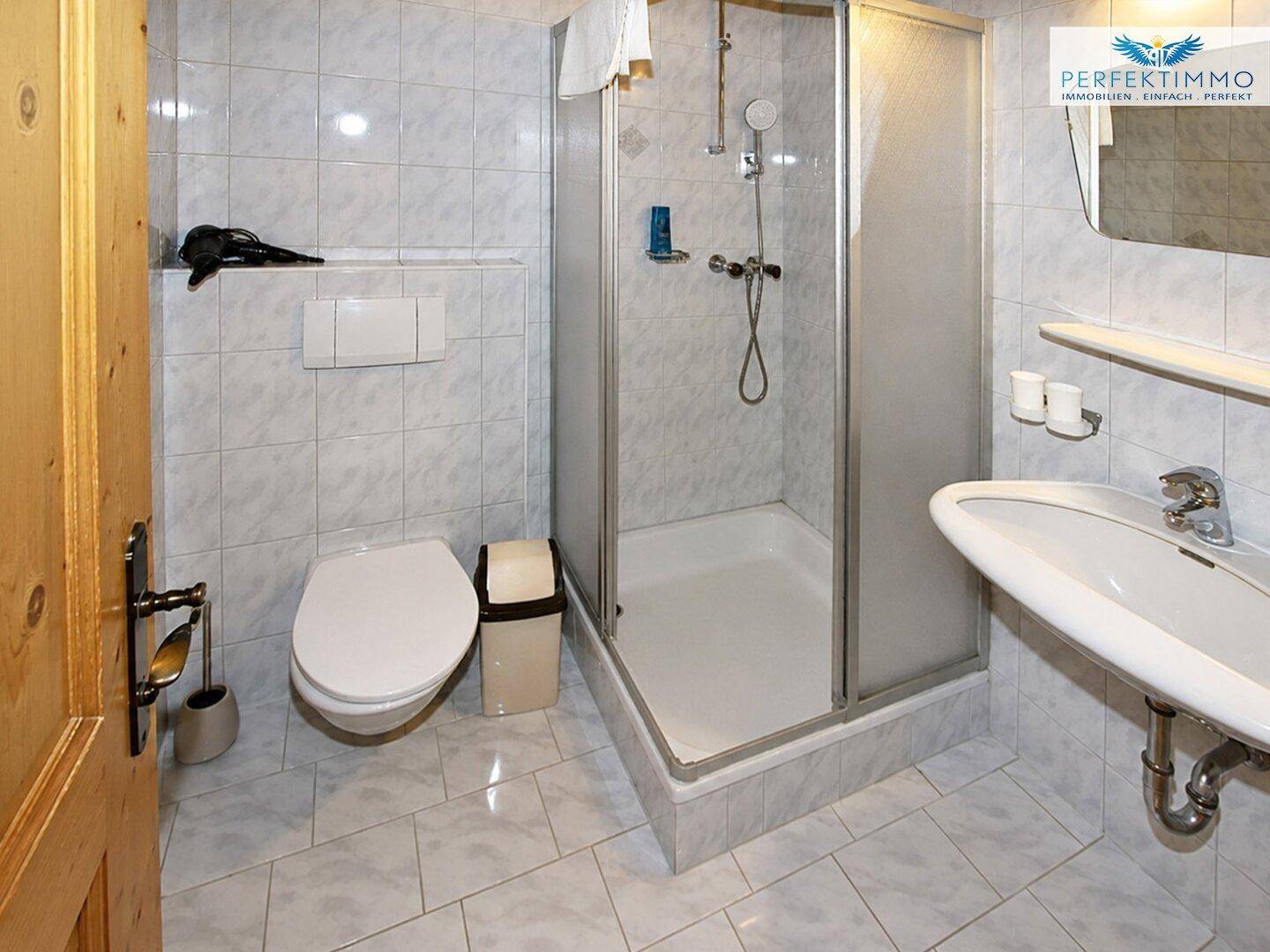 Helles Badezimmer mit Dusche, WC und Waschbecken, ausgestattet mit weißen Fliesen.