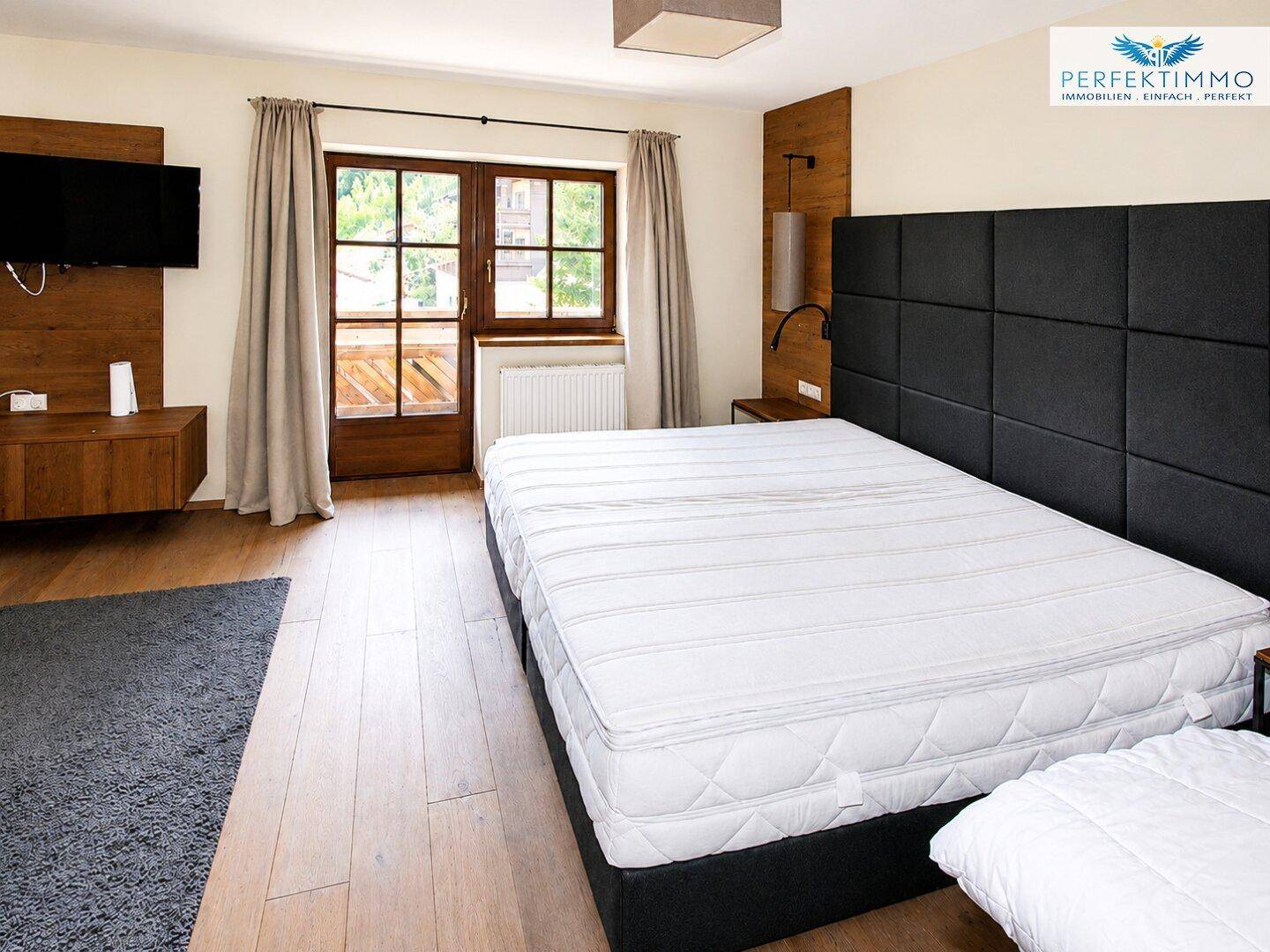 Modernes Schlafzimmer mit großem Bett, Holzboden und Zugang zum Balkon.