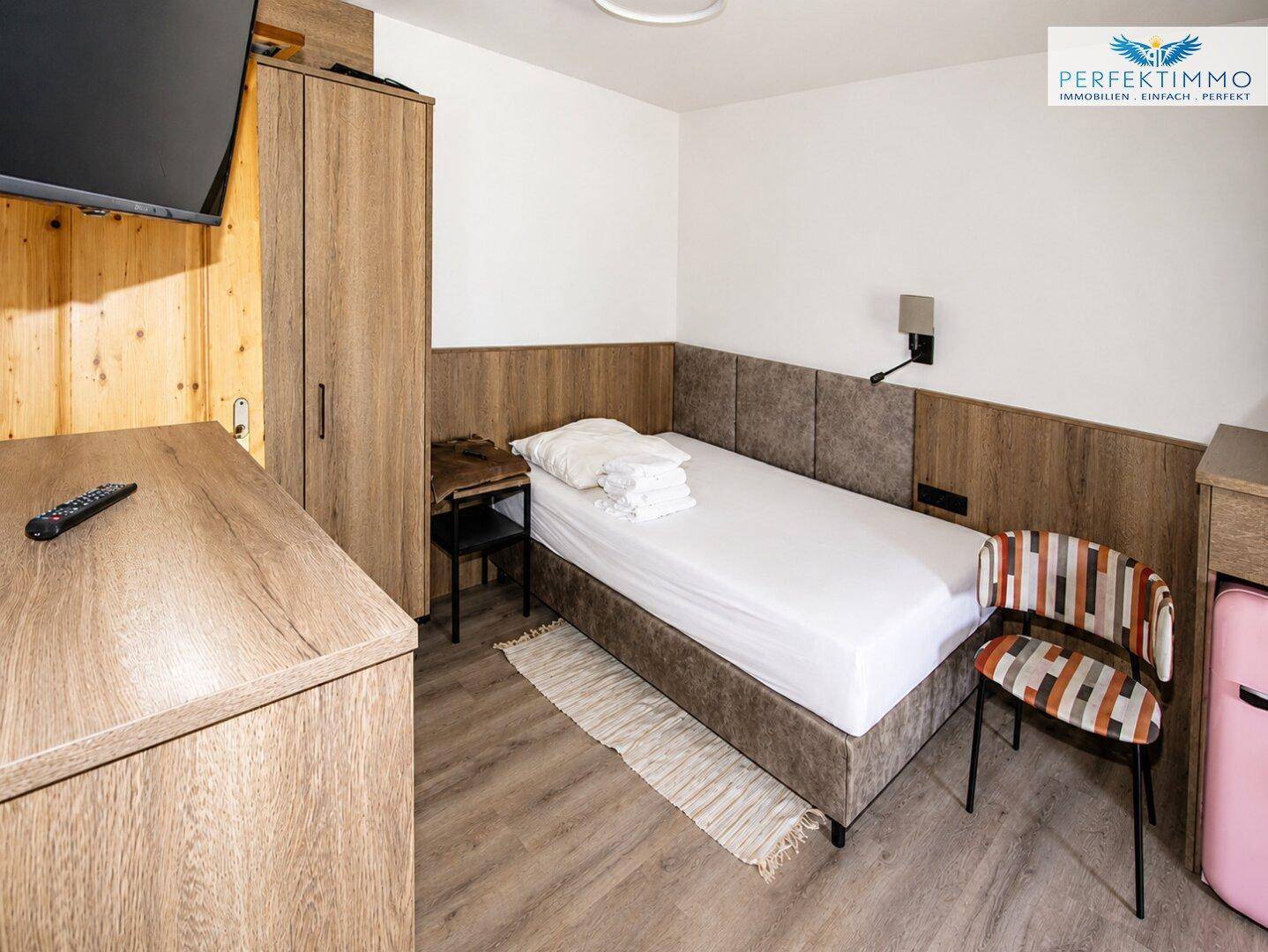 Gemütliches Einzelzimmer mit Holzwänden, Bett und Schreibtisch.