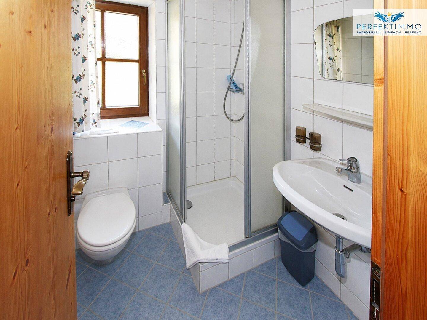 Helles Badezimmer mit Dusche, WC und Waschbecken, ausgestattet mit blauen und weißen Fliesen.