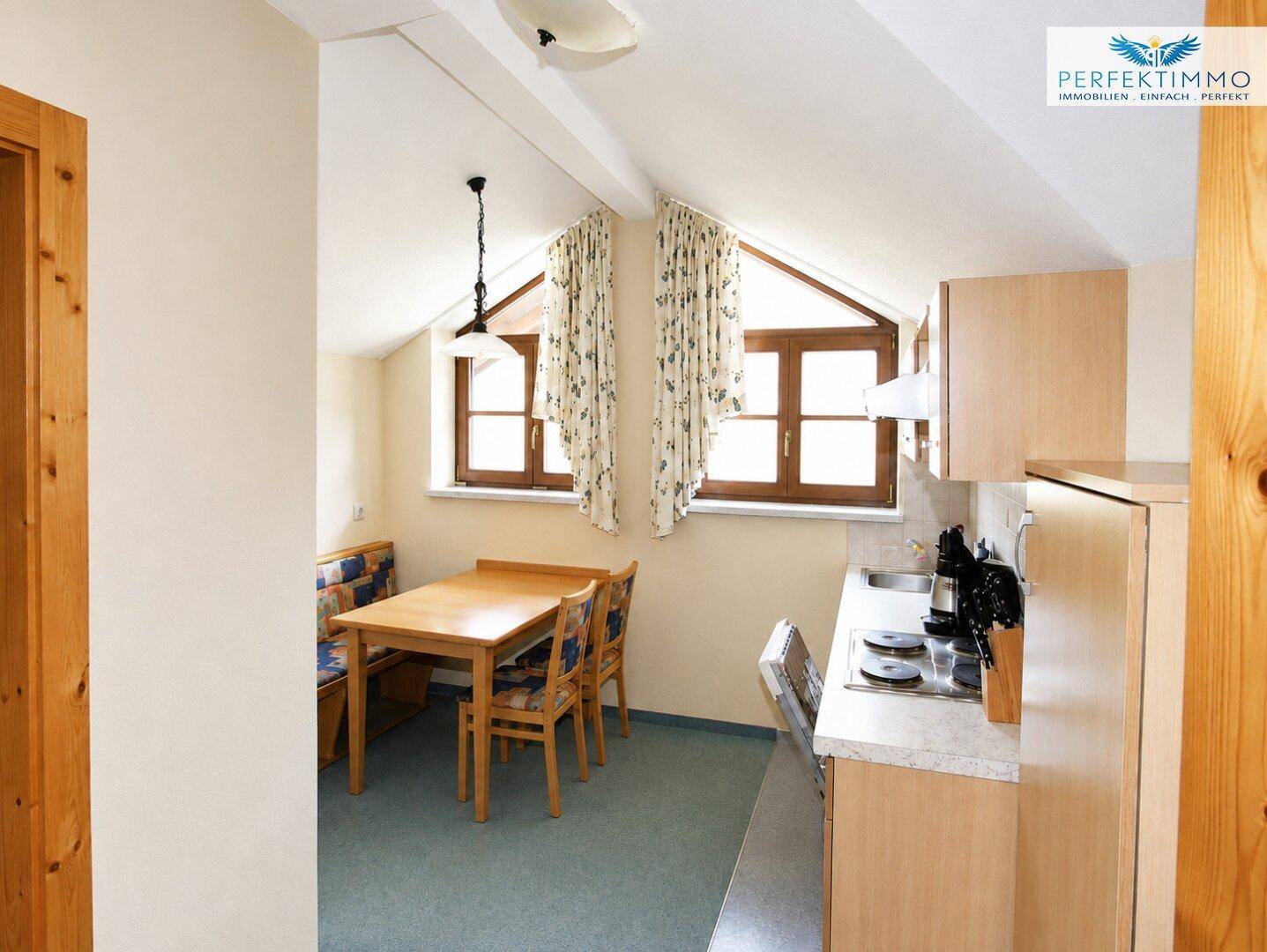 Gemütliche Küche mit Essbereich unter Dachschrägen und Holzfenstern, ideal für kleine Mahlzeiten.