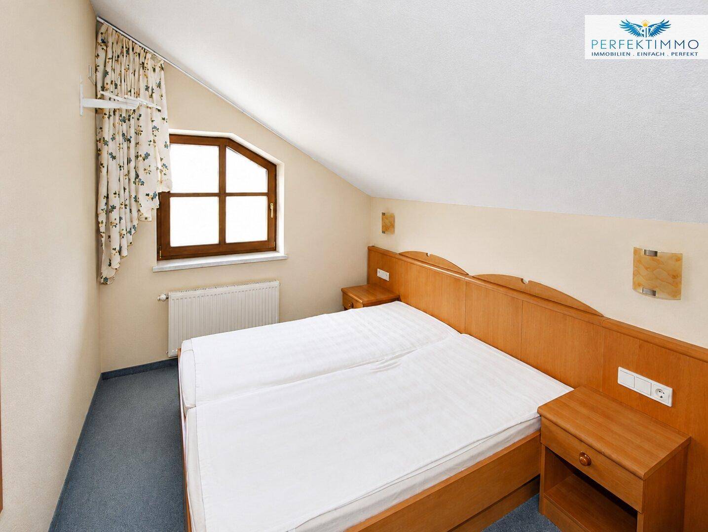 Helles Schlafzimmer mit zwei Einzelbetten, Holzmöbeln und Dachschrägenfenster für natürliche Belichtung.