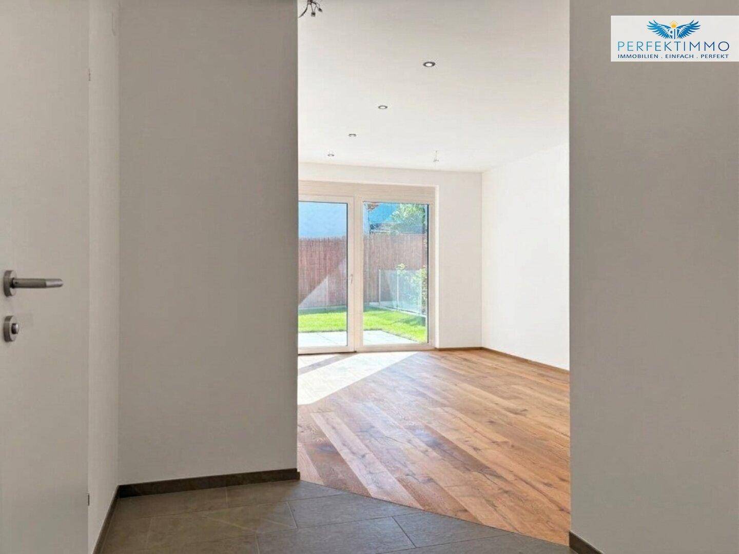 Übergangsbereich vom Flur mit Fliesenboden zu einem hellen Raum mit Holzboden und Gartenzugang.