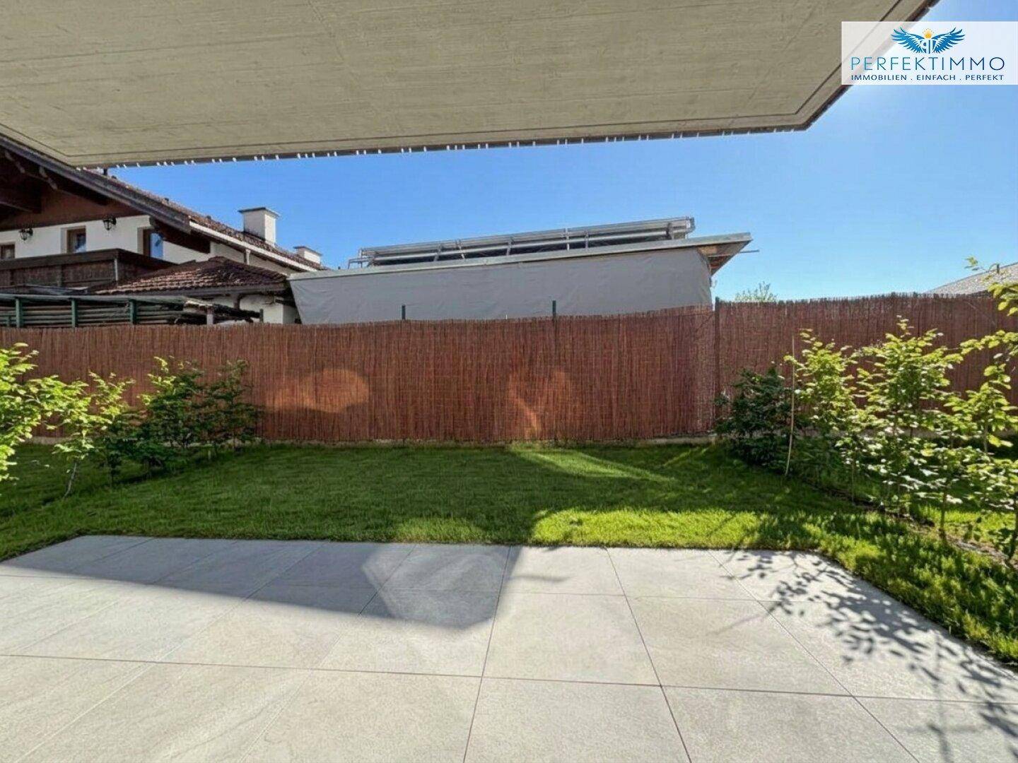 Sonniger Terrassenbereich mit modernen Fliesen und kleinem Rasenstück, umgeben von einem Sichtschutz.