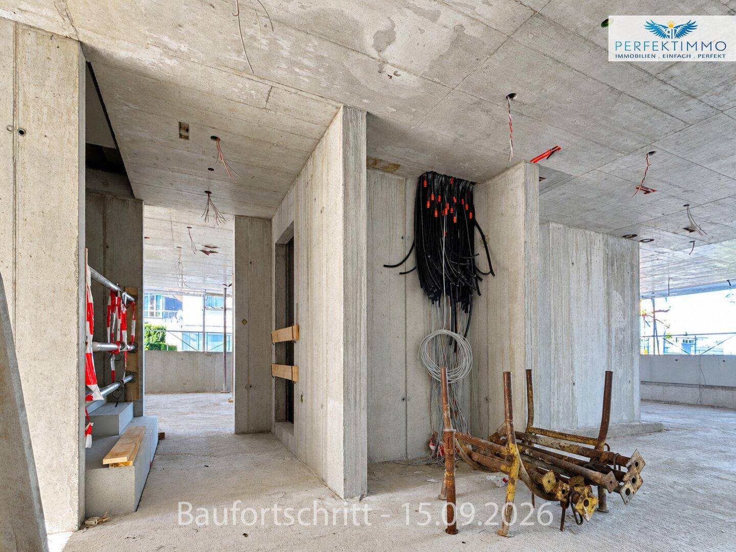 Unfertiger Innenraum eines Neubaus mit rohen Betonwänden und Decken sowie sichtbaren Elektroinstallationen.