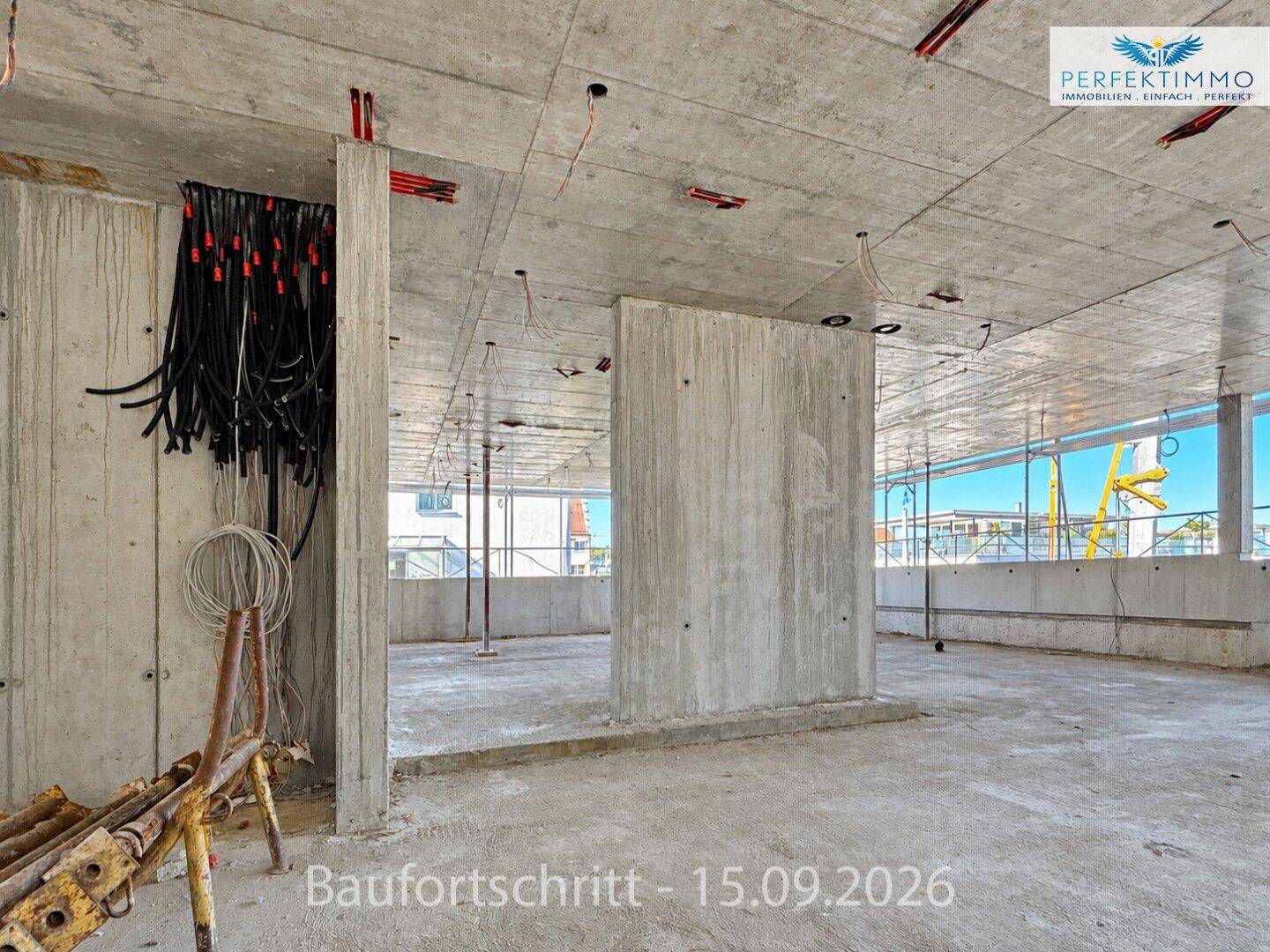 Großer, offener Innenraum im Rohbau mit Betonwänden, Decken und vorbereiteten Elektroanschlüssen.