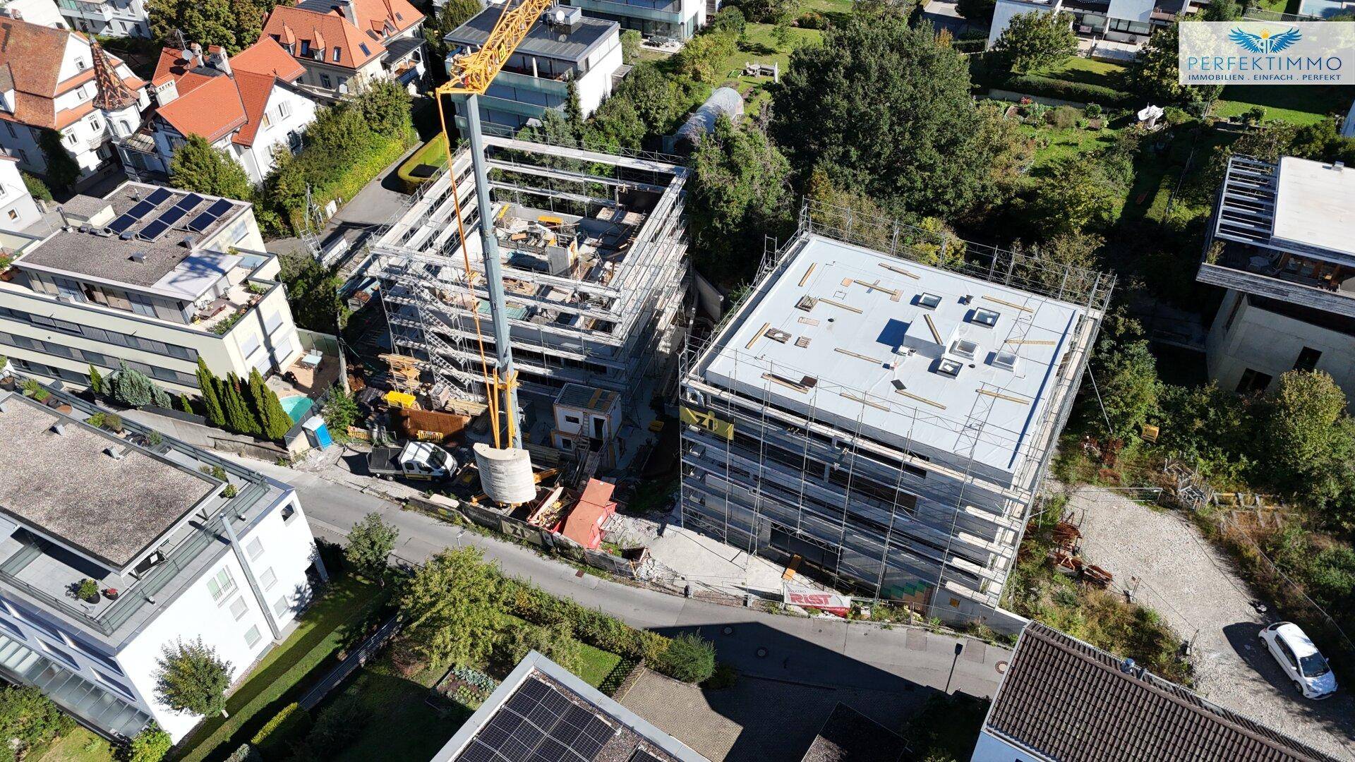 Luftaufnahme einer Baustelle mit zwei im Bau befindlichen Gebäuden und einem Kran in einer Wohngegend.