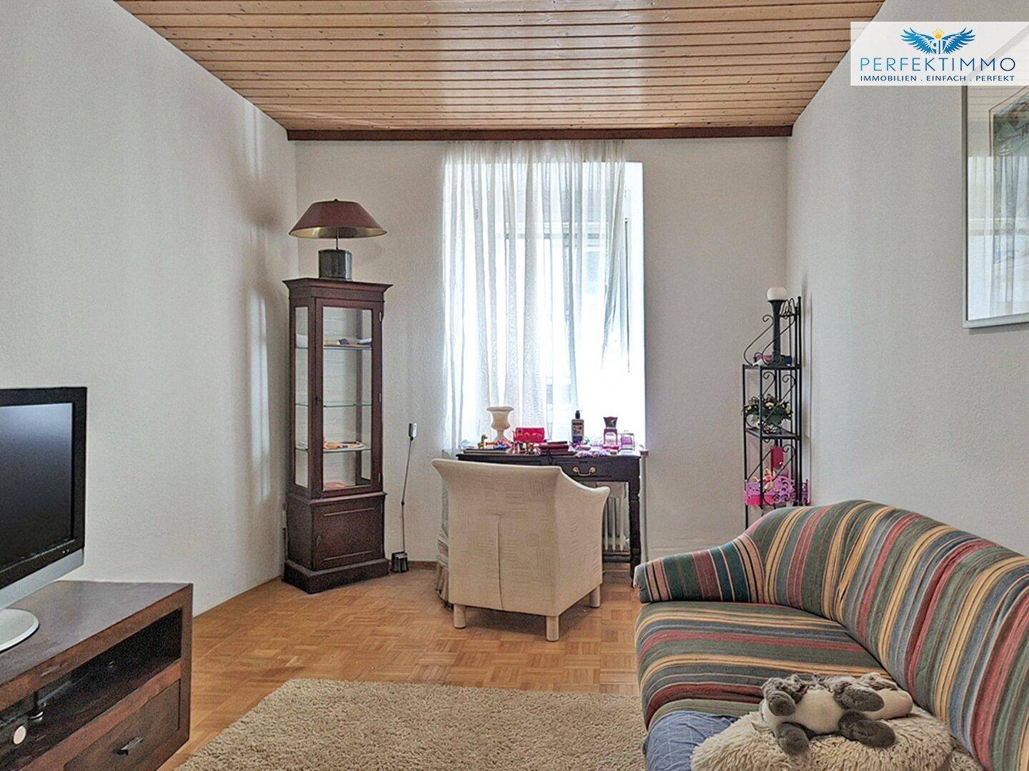 Gemütliches Wohnzimmer mit gestreiftem Sofa, Holzdecke und Parkettboden.