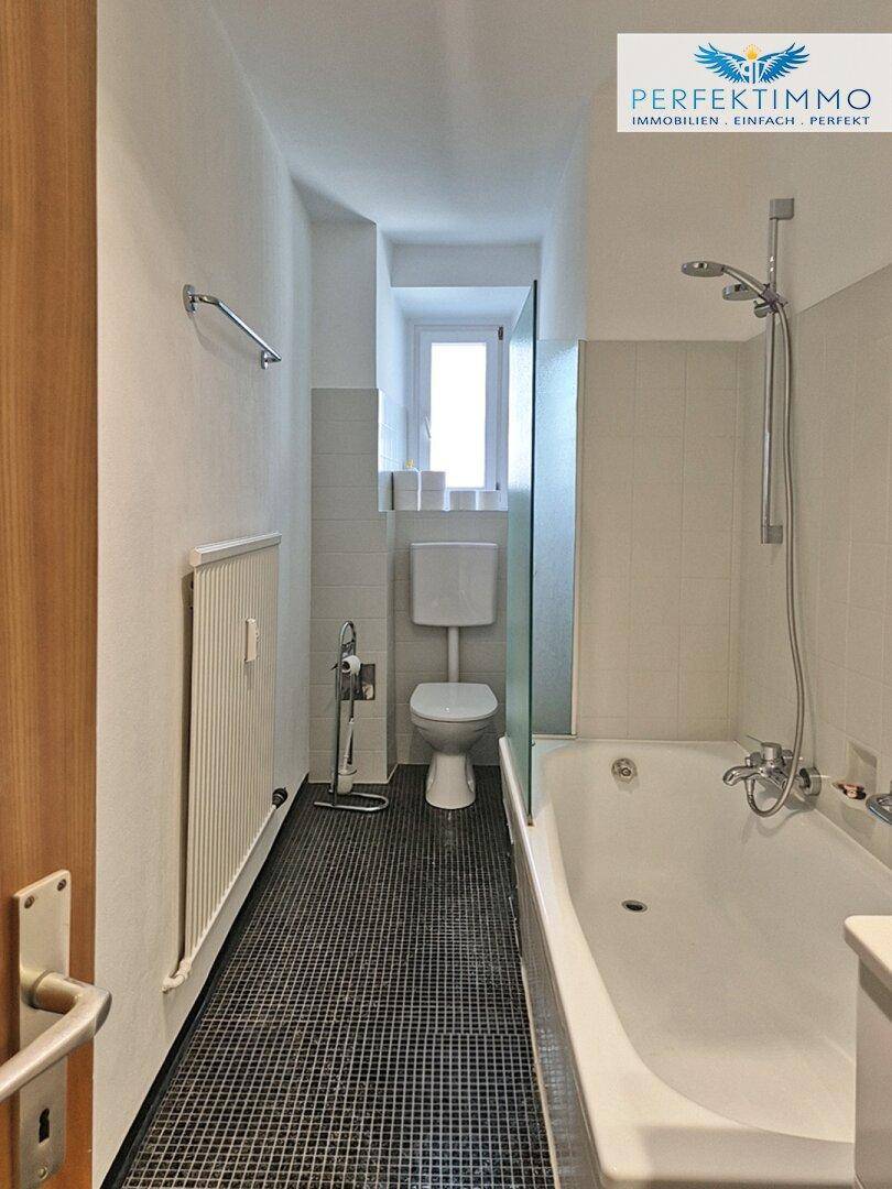 Langes, schmales Badezimmer mit Badewanne, Dusche und kleinen Mosaikfliesen am Boden.