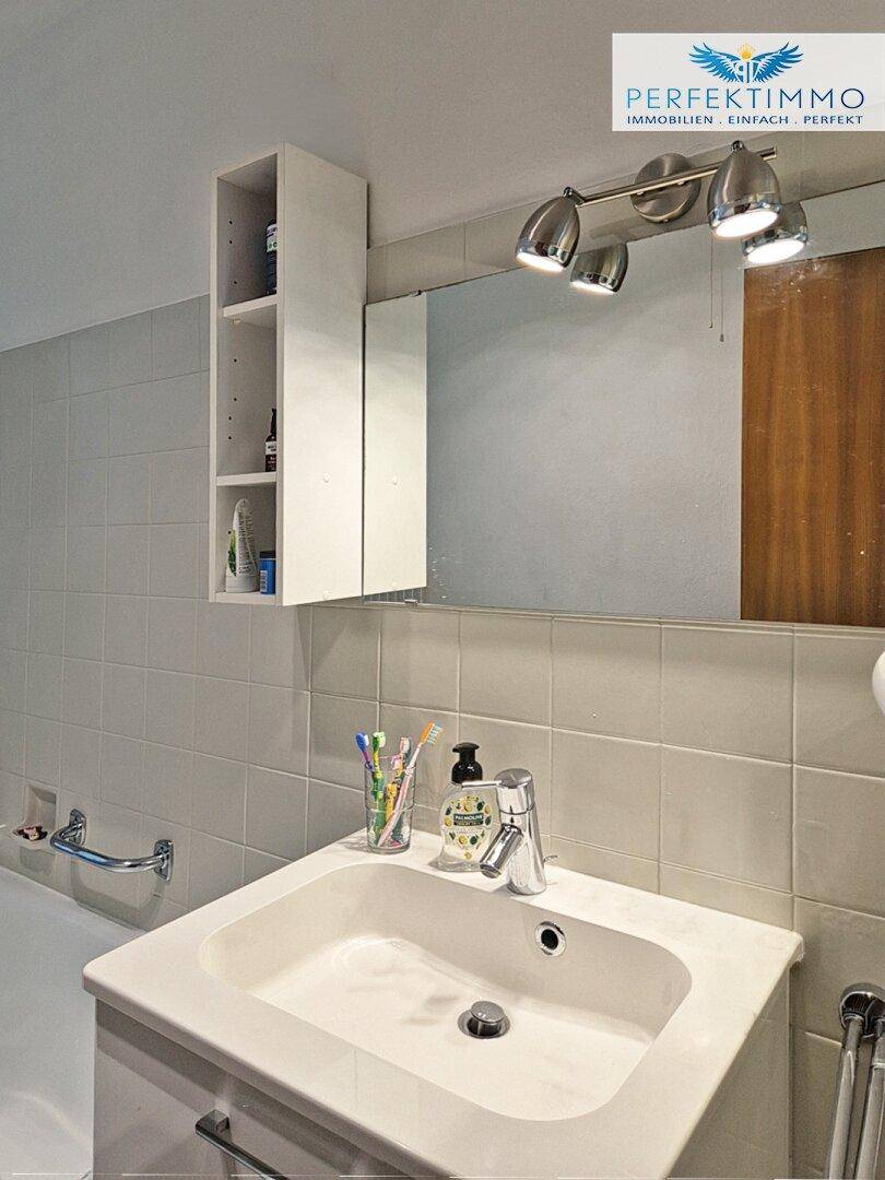 Waschbecken mit Spiegelschrank und Beleuchtung in einem hell gefliesten Badezimmer.