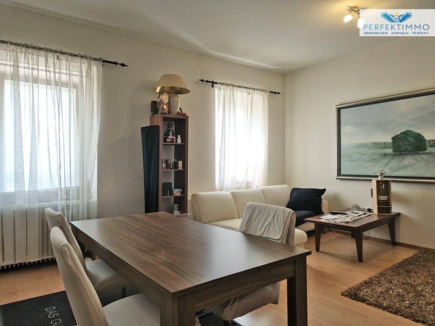 Heller Wohn- und Essbereich mit Holztisch, Sofa und Parkettboden.