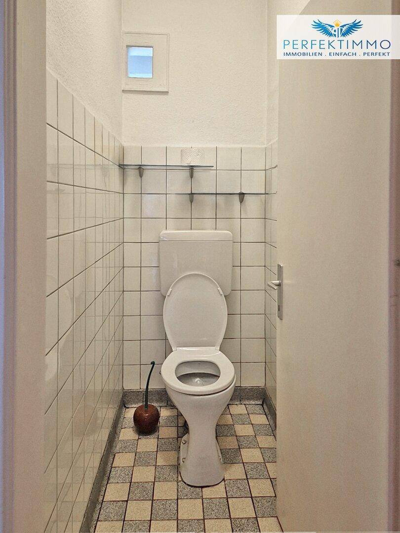 Separate Toilette mit weißen Fliesen und kleinem Fenster für Belüftung.