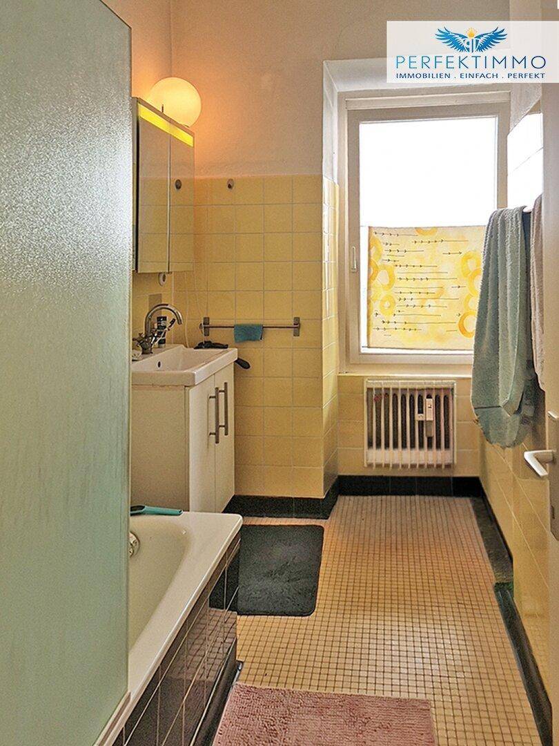 Badezimmer mit gelben Fliesen, Badewanne und Fenster, das Tageslicht hereinlässt.
