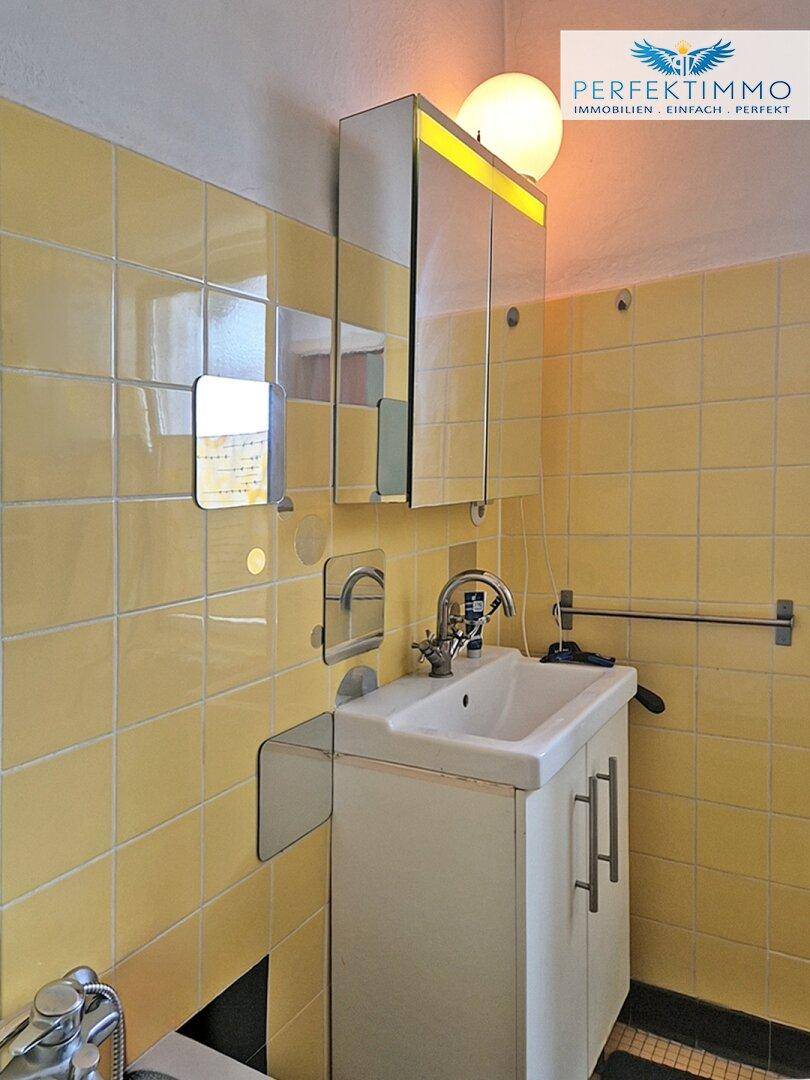 Waschbecken mit Spiegelschrank und gelben Fliesen in einem Badezimmer.