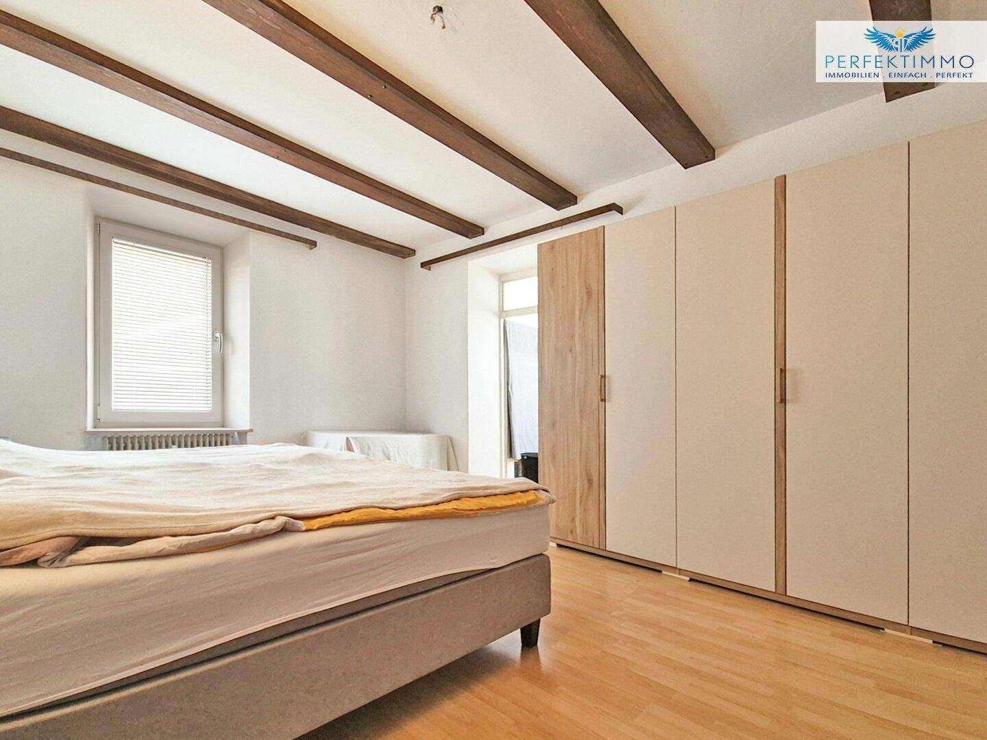 Schlafzimmer mit Holzbalken an der Decke, Doppelbett und Einbauschränken.