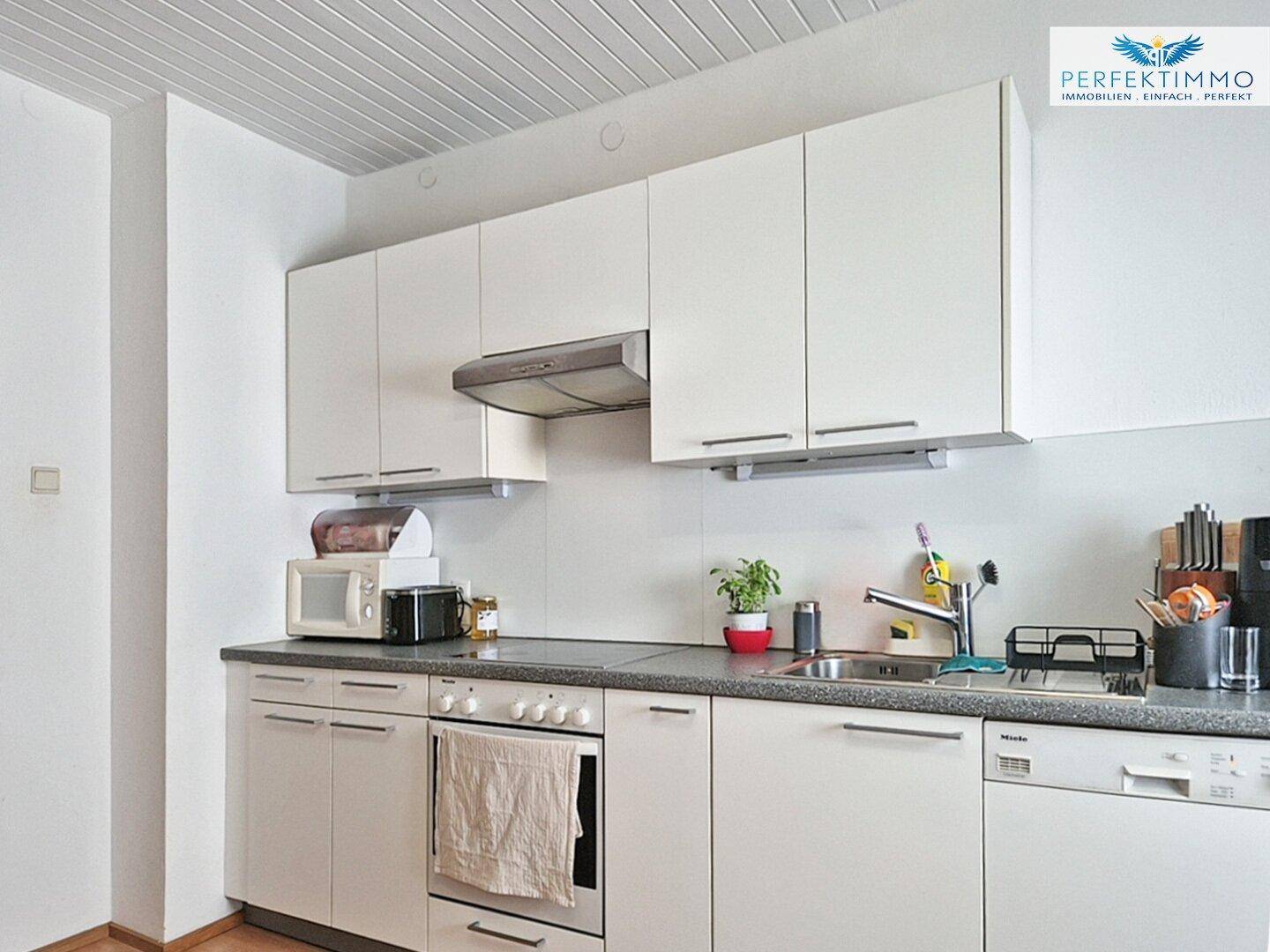 Moderne Einbauküche mit weißen Schränken, Mikrowelle und Geschirrspüler.