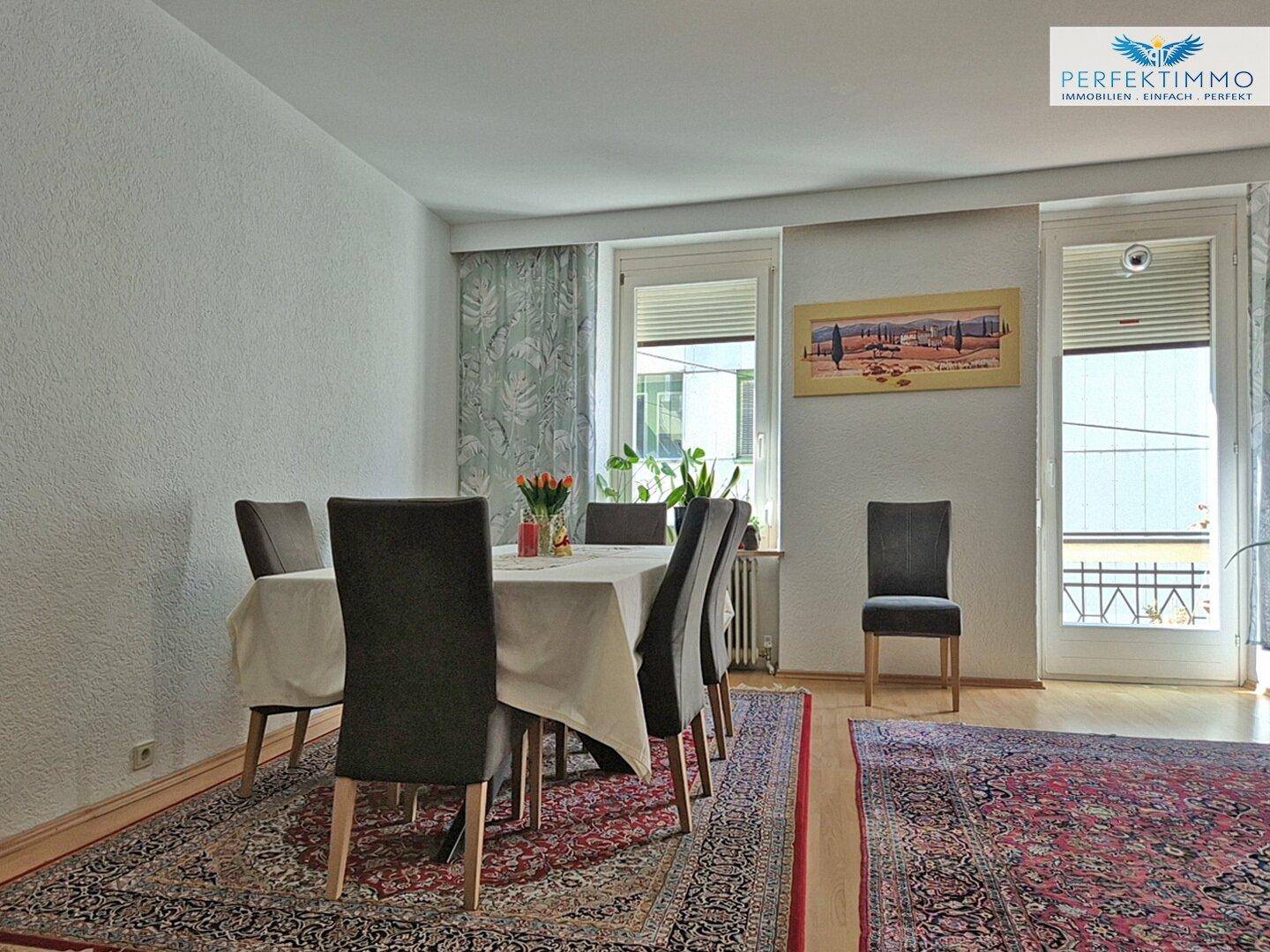Essbereich mit großem Holztisch, Teppich und Zugang zu einem französischen Balkon.