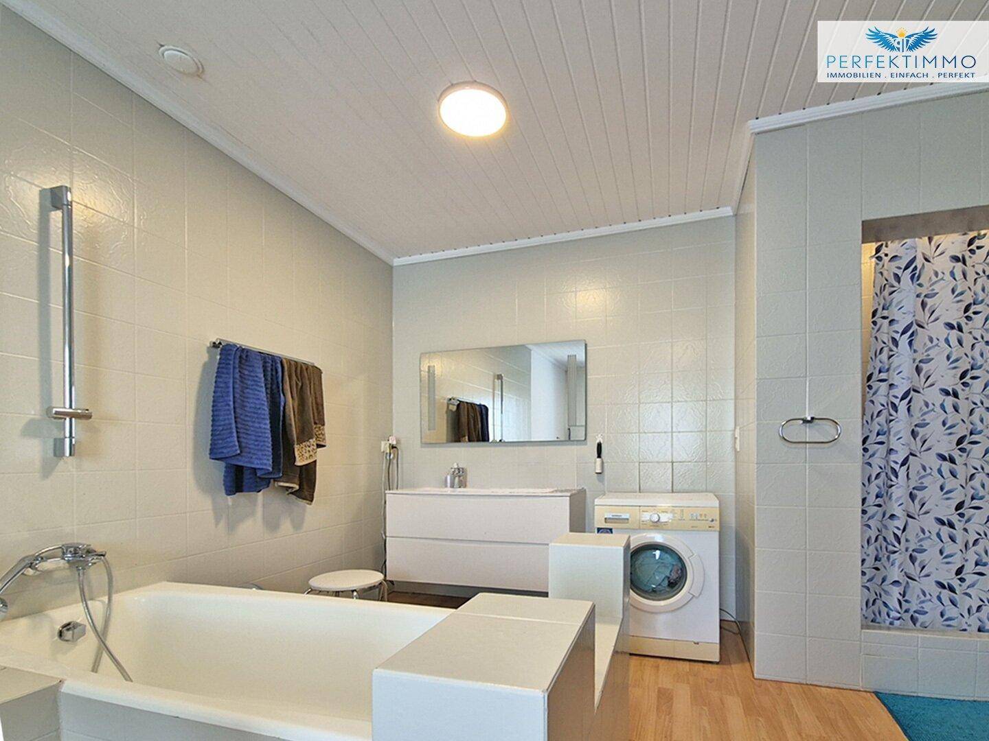 Helles Badezimmer mit Badewanne, Duschvorhang und Waschmaschine.