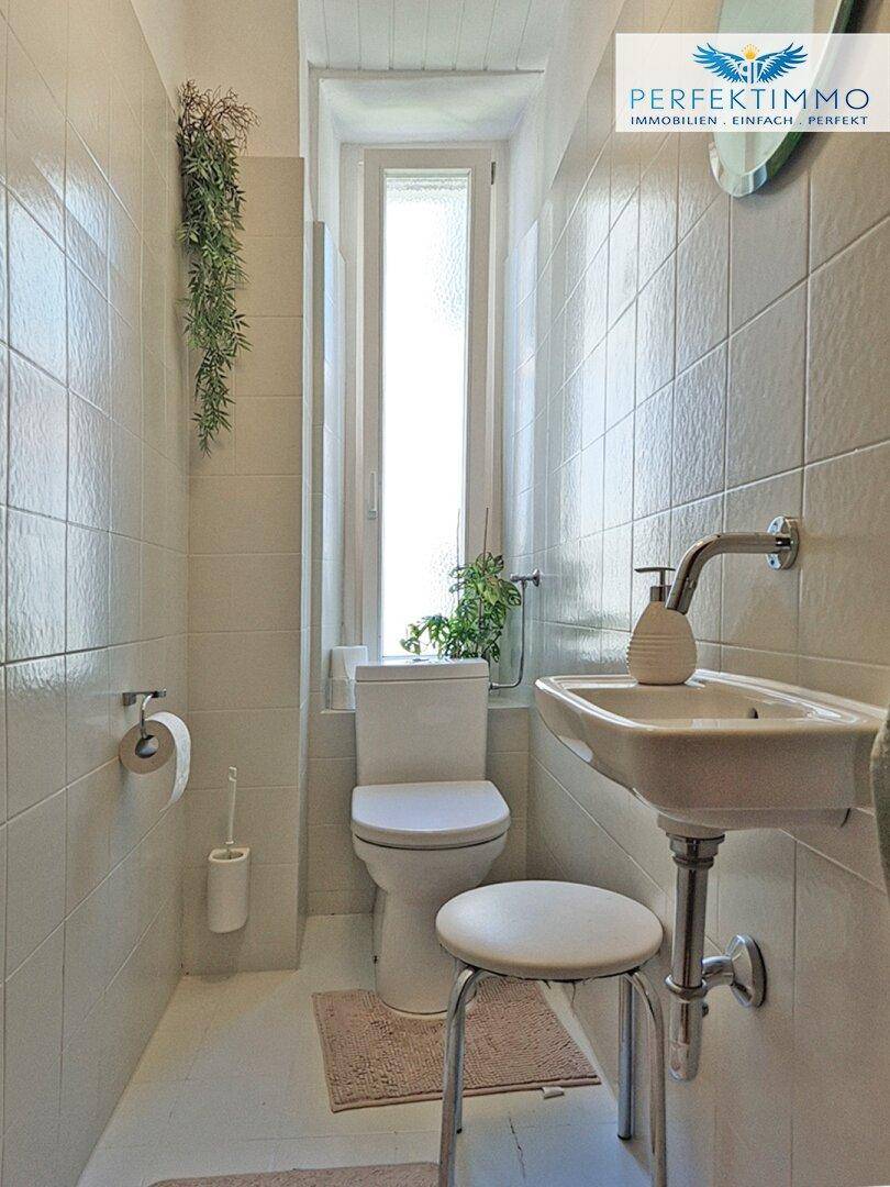 Separate Toilette mit Fenster, Waschbecken und Wandfliesen.