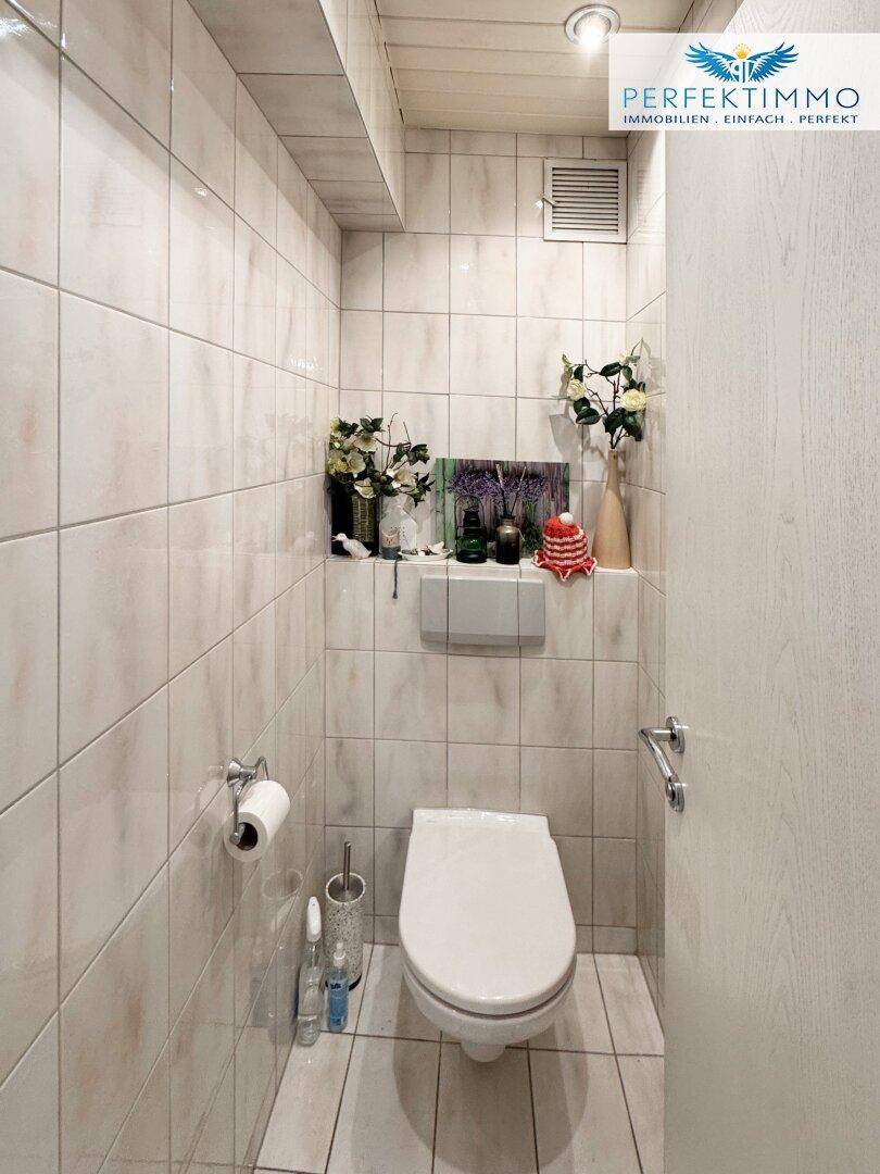Separate Toilette mit Wand-WC und hellen Fliesen an Wänden und Boden.