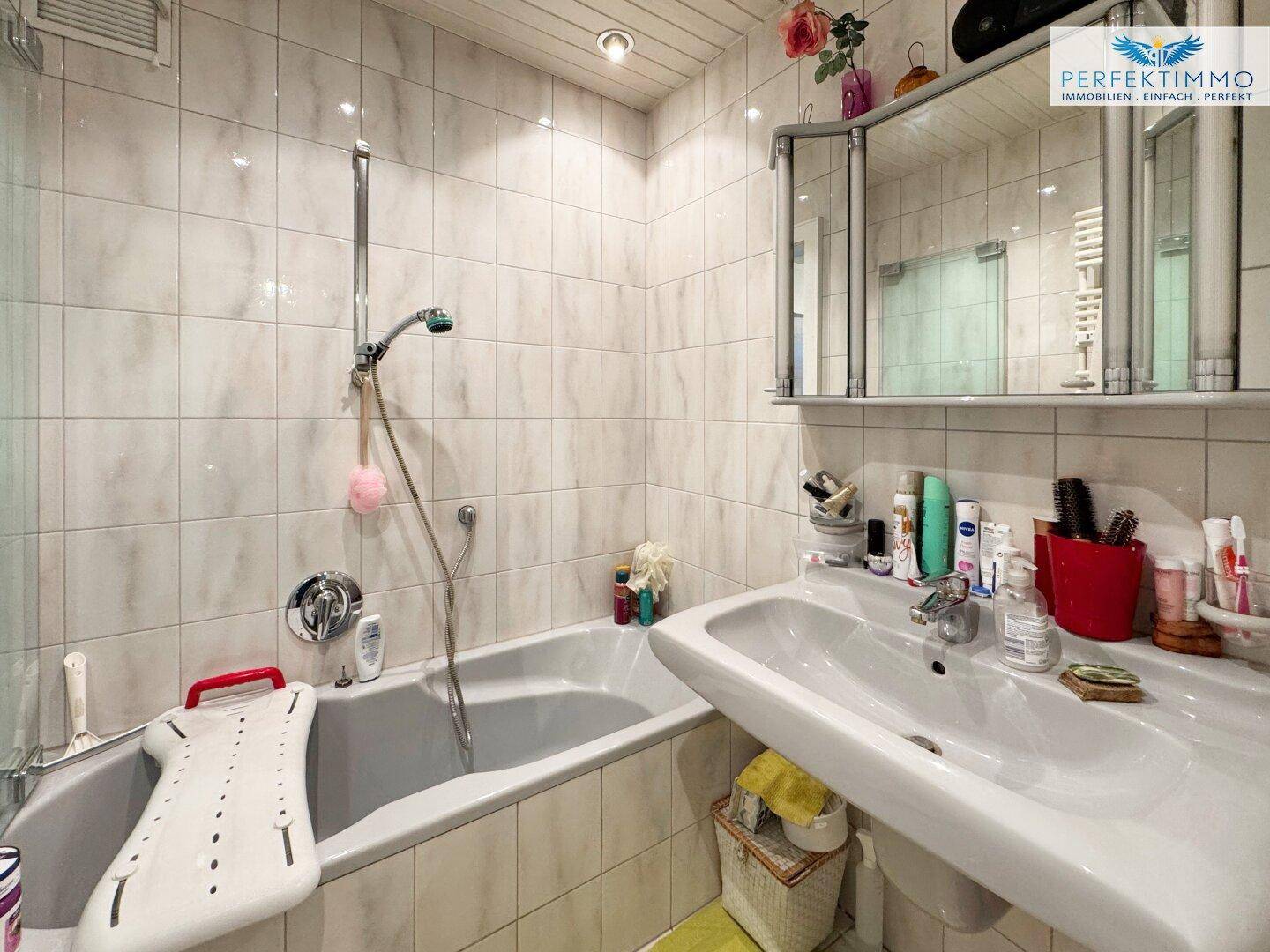 Gefliestes Badezimmer mit Badewanne, Waschbecken und Spiegelschrank.