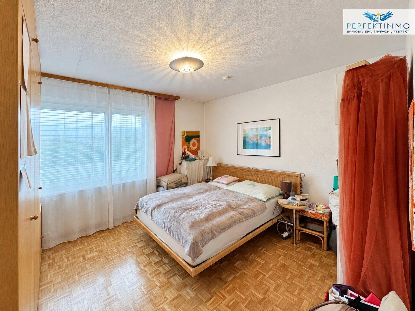 Schlafzimmer mit Doppelbett, Holzparkett und großem Fenster für viel Tageslicht.