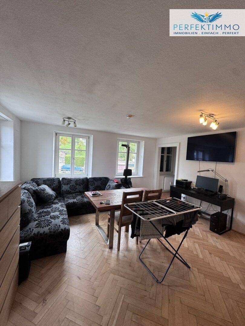 Gemütlicher Wohn-Essbereich mit Fischgrätparkett, großem Sofa und Esstisch, hell durch Fenster.