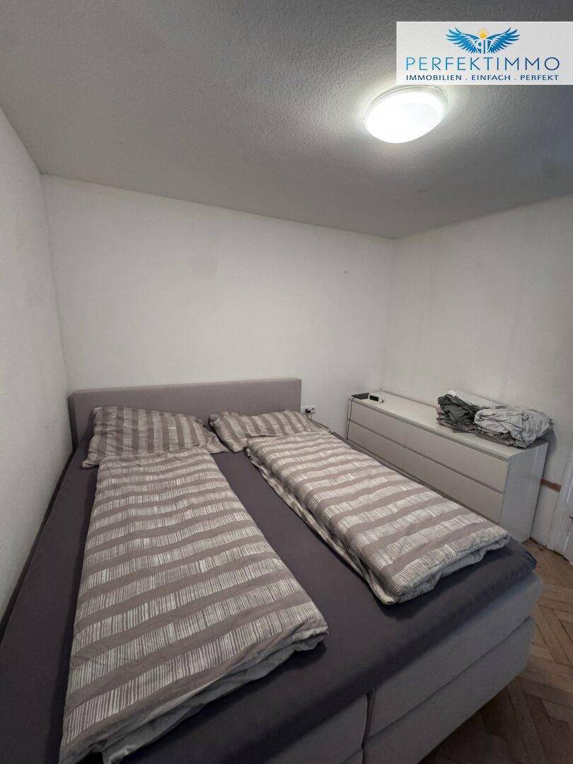 Schlafzimmer mit Doppelbett und schlichter Einrichtung, hell gestrichene Wände und Parkettboden.
