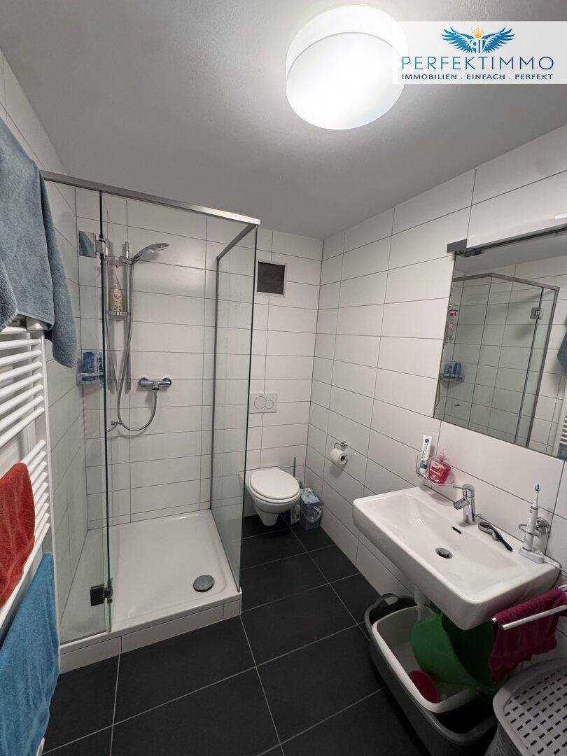 Modernes Badezimmer mit weißen Fliesen, dunklem Boden und Glasdusche, ausgestattet mit Handtuchheizkörper.