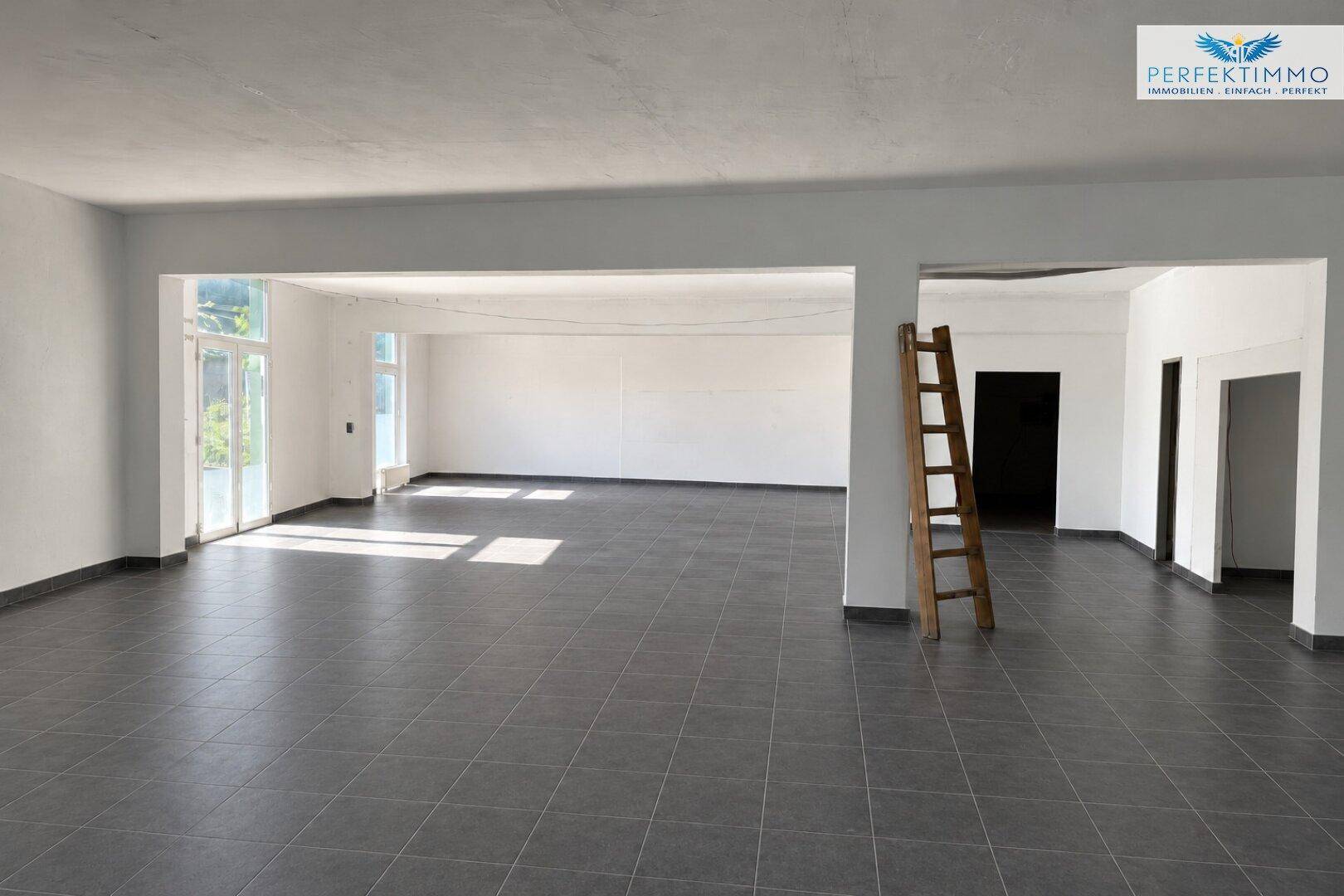 Großer, offener Gewerberaum mit viel Tageslicht und einer Holzleiter, ideal für flexible Nutzung.