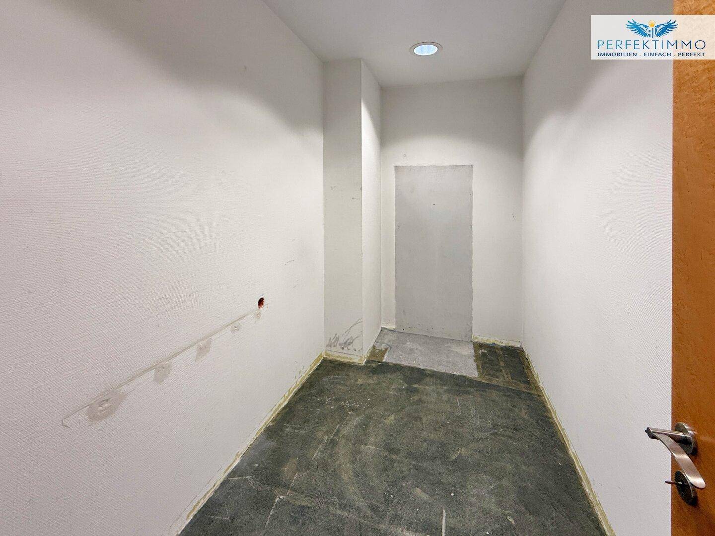 Schmaler Flur oder Abstellraum mit weißen Wänden und einfachem Bodenbelag, bereit zur Renovierung.
