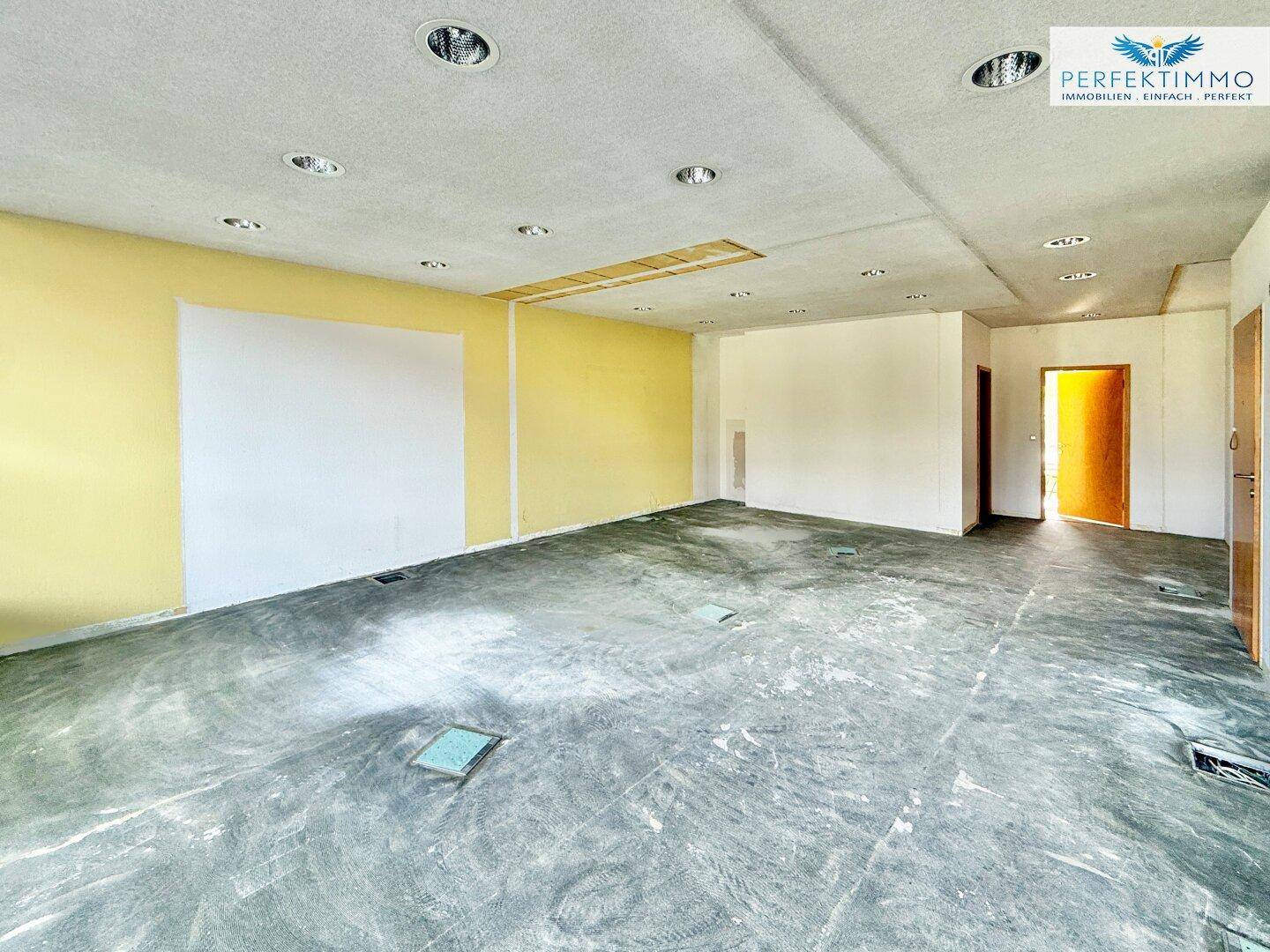 Geräumiger Gewerberaum mit gelben Akzentwänden und Einbauleuchten in der Decke, bietet viel Potenzial.