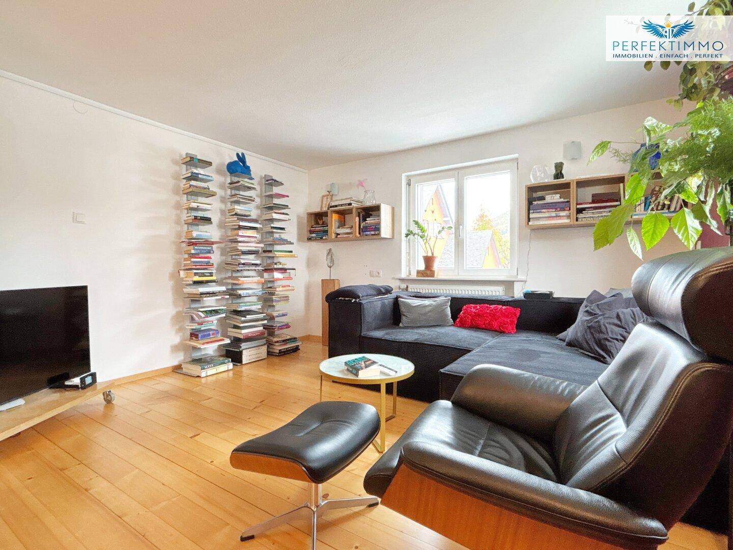 Gemütliches Wohnzimmer mit Holzboden, großem Sofa und Bücherregalen an der Wand.