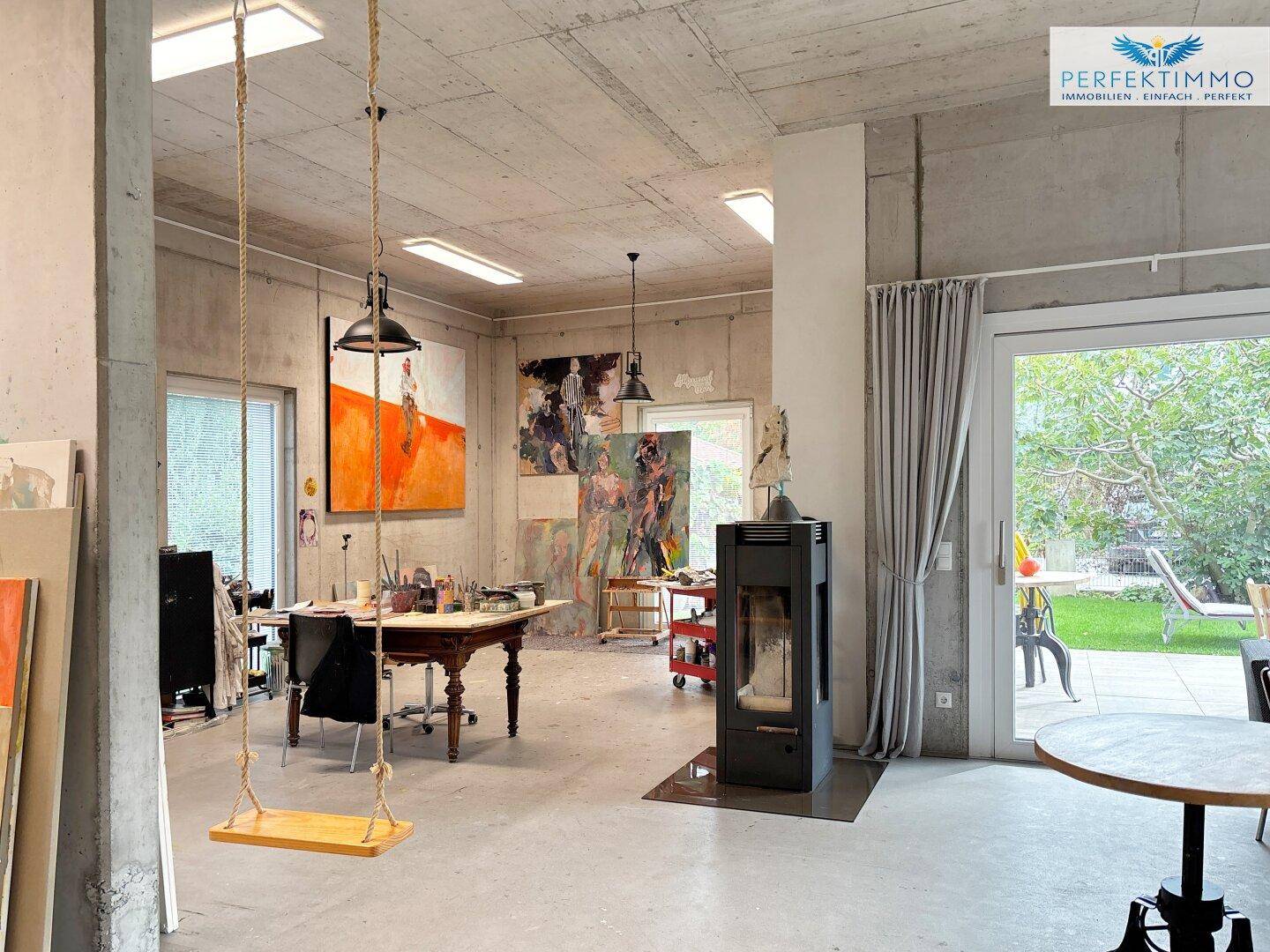 Helles Atelier mit Betonwänden, Kaminofen, Schaukel und Zugang zum Garten.