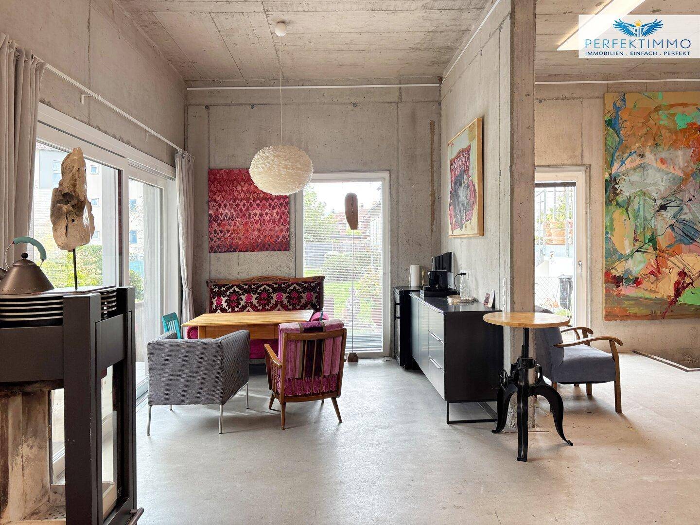 Offener Wohnbereich mit verschiedenen Sitzgelegenheiten, Kunstwerken und großen Fenstern.