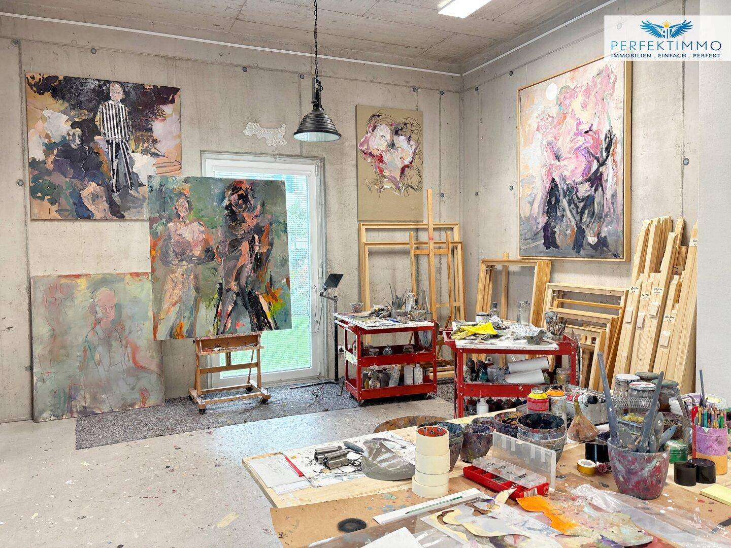 Kreatives Atelier mit zahlreichen Kunstwerken, Staffeleien und Arbeitsmaterialien in einem Loftraum.