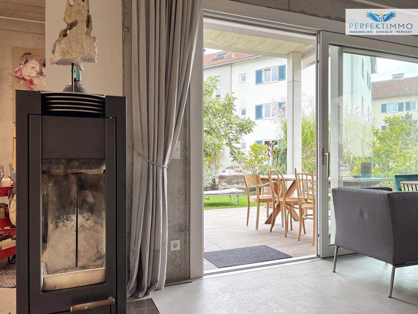 Wohnbereich mit Kaminofen und großen Schiebetüren, die zur Terrasse und zum Garten führen.