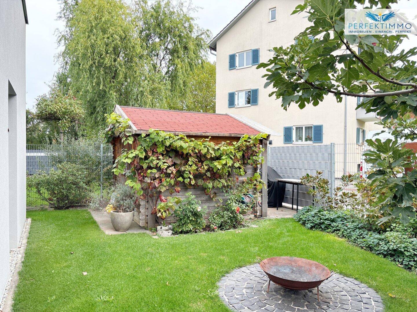 Idyllischer Garten mit Gartenhaus, Feuerstelle und Grillbereich, umgeben von Grün.