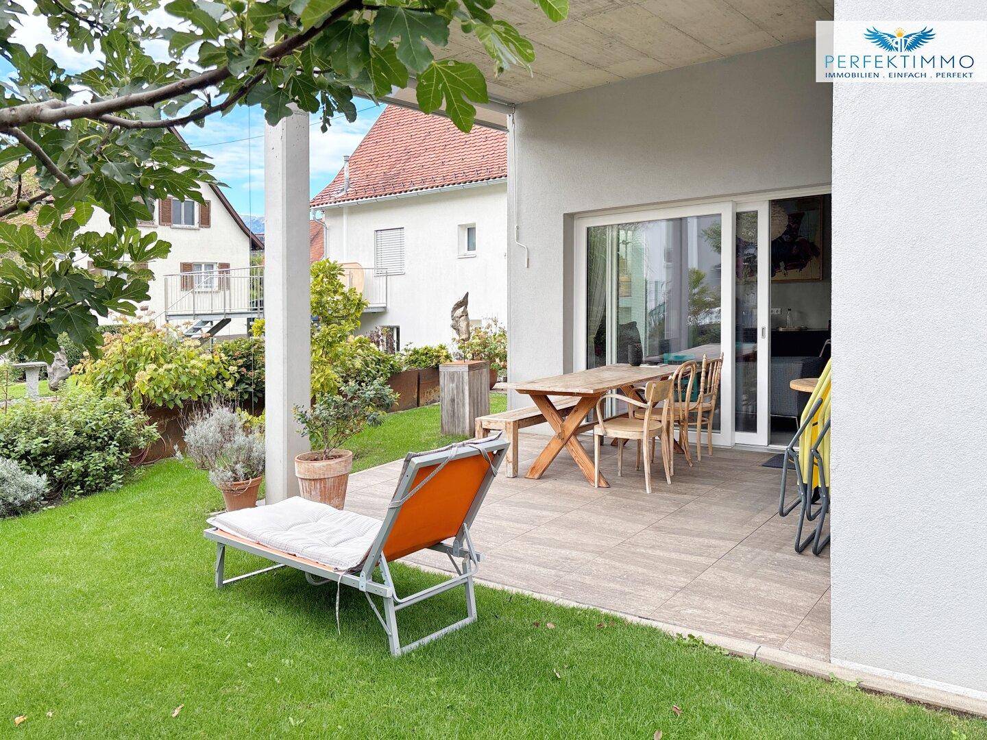 Große, geflieste Terrasse mit Esstisch, Sonnenliege und Blick auf den Garten.