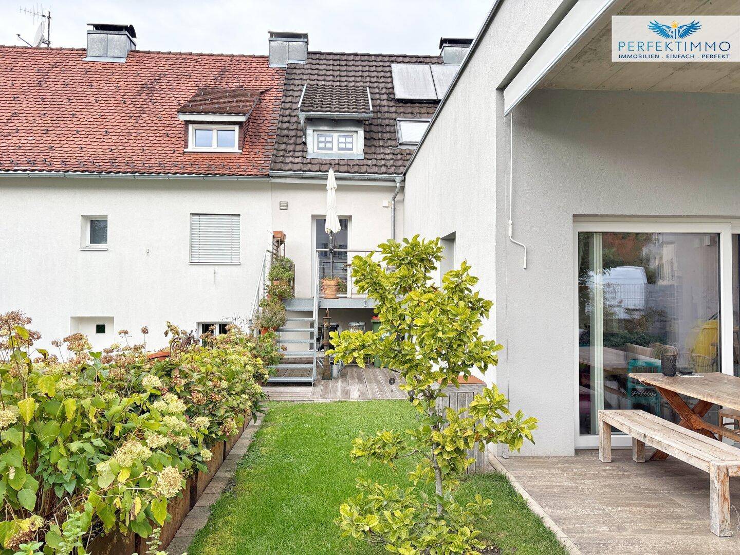 Gepflegter Gartenbereich mit Rasenfläche, Blumenbeeten und einer kleinen Holzterrasse.