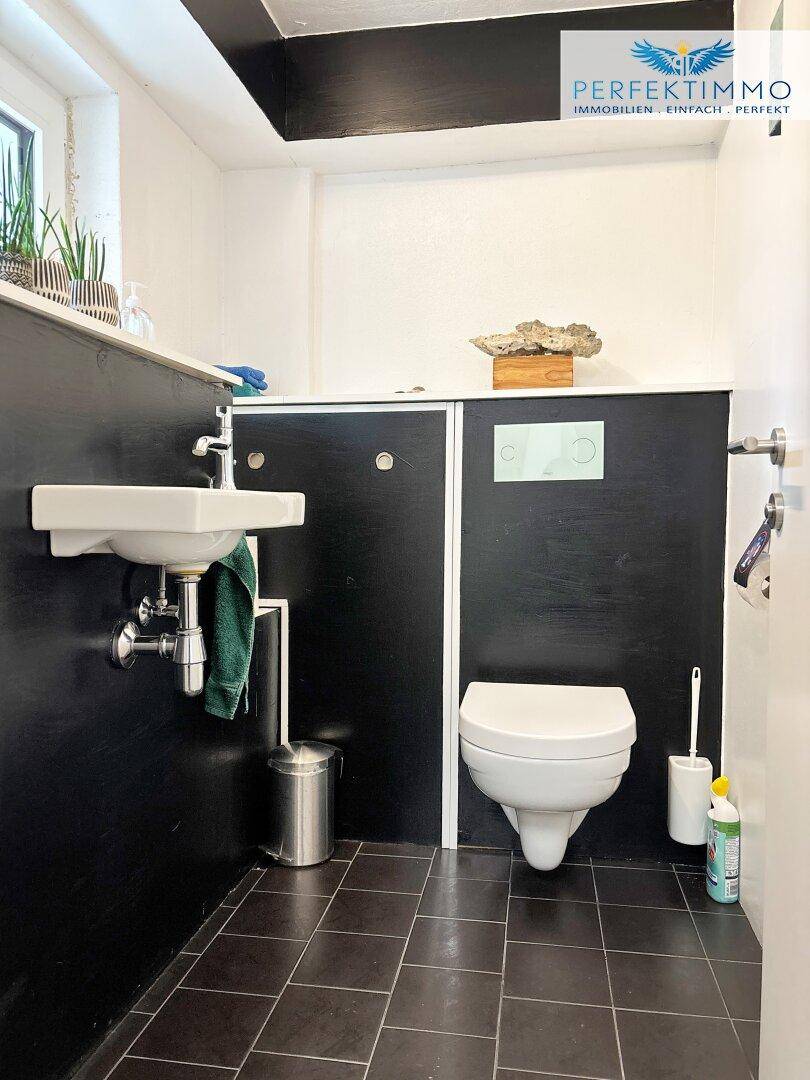 Kleines Gäste-WC mit schwarzer Wandverkleidung, weißem Waschbecken und dunklen Fliesen.
