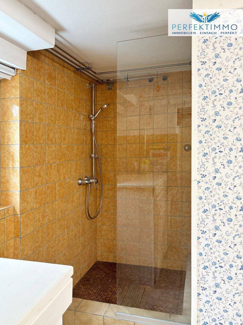 Badezimmer mit Duschkabine, orangefarbenen Fliesen und floraler Tapete.