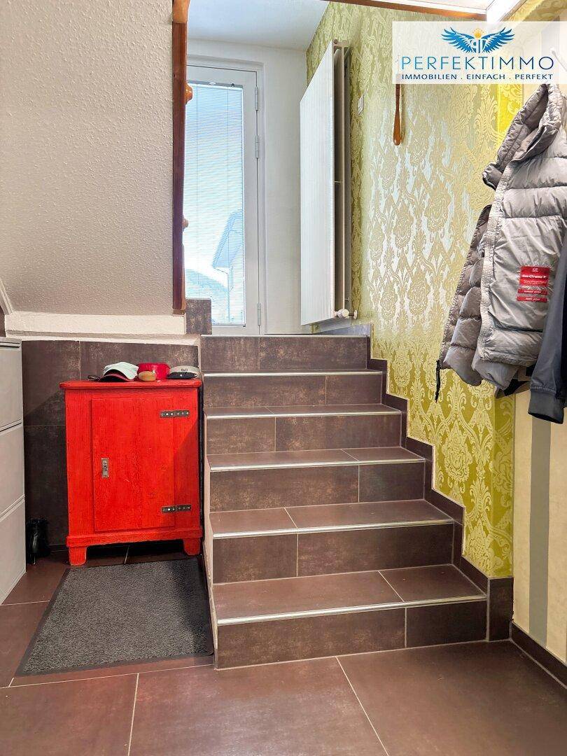 Treppenaufgang mit gemusterten Tapeten und Fliesenboden, der zu einem Ausgang führt.