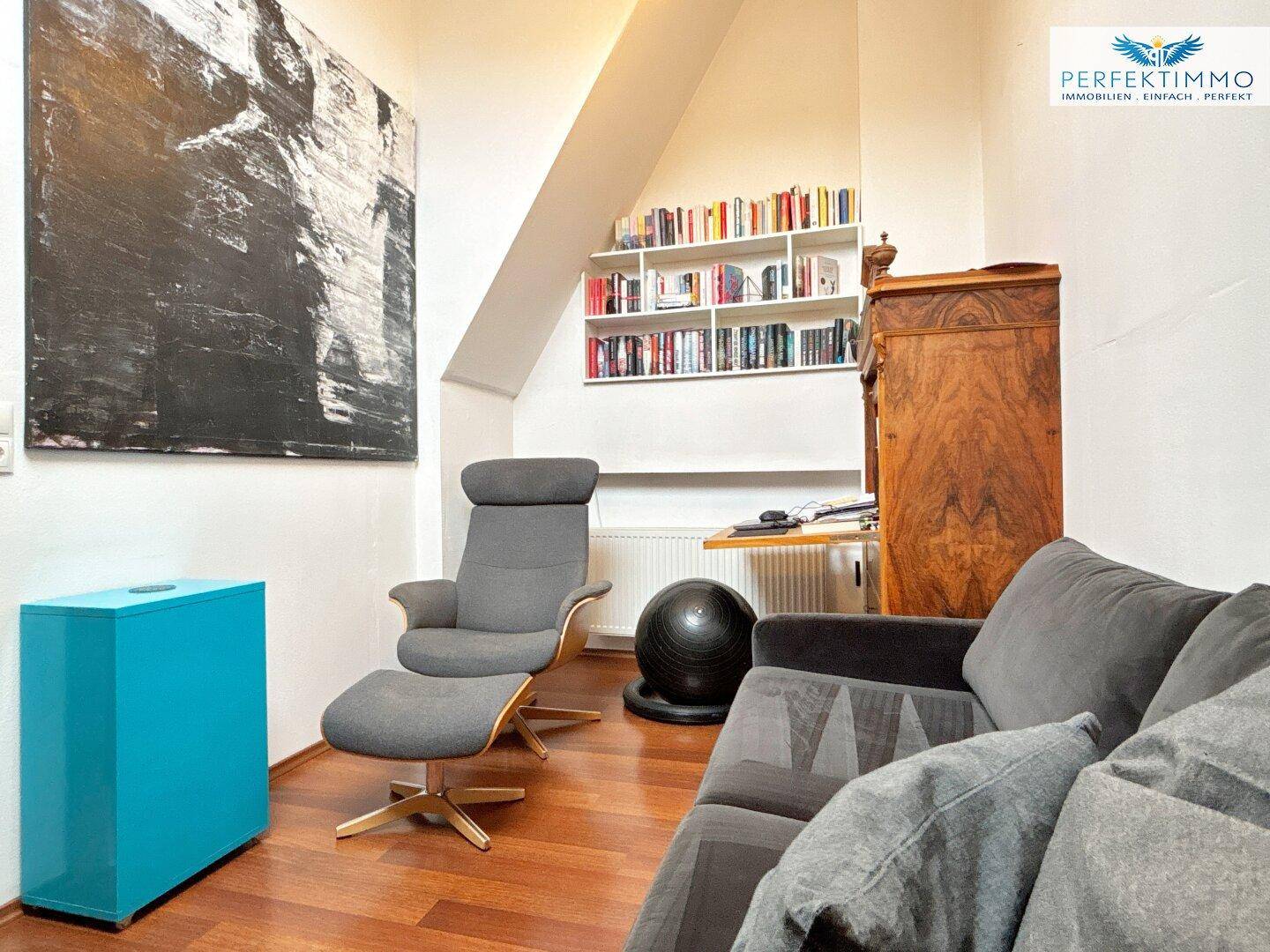 Gemütlicher Wohnbereich im Dachgeschoss mit Sofa, Sessel und Bücherregal.