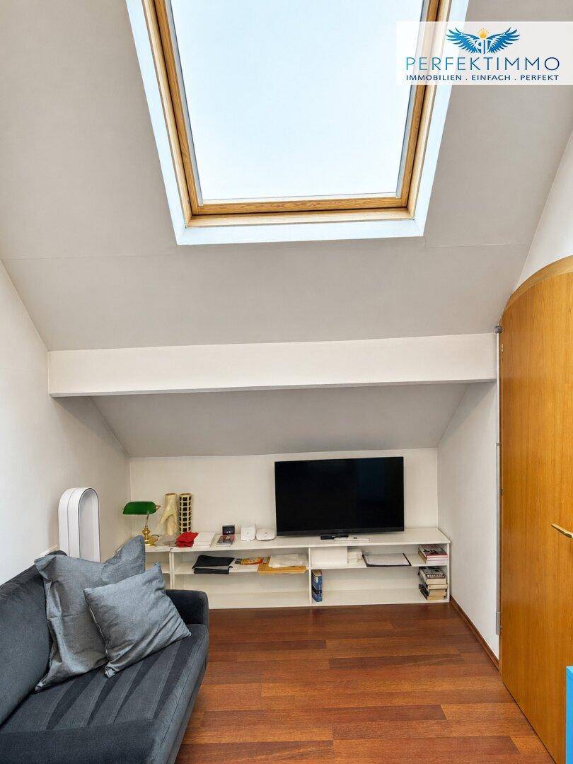 Moderner Wohnbereich im Dachgeschoss mit Fernseher, Sofa und großem Dachfenster.