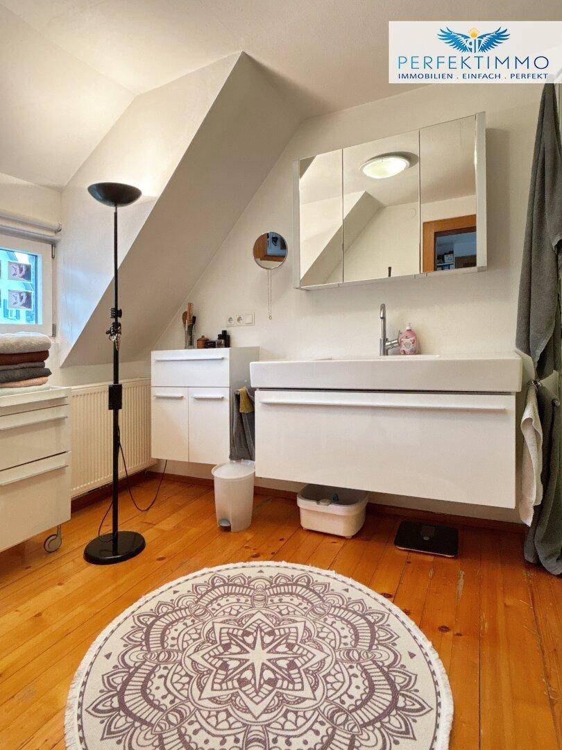 Helles Badezimmer im Dachgeschoss mit modernem Waschtisch, Spiegelschrank und Holzboden.