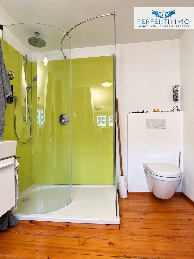 Modernes Badezimmer mit begehbarer Dusche, hellgrünen Wänden und Holzboden.