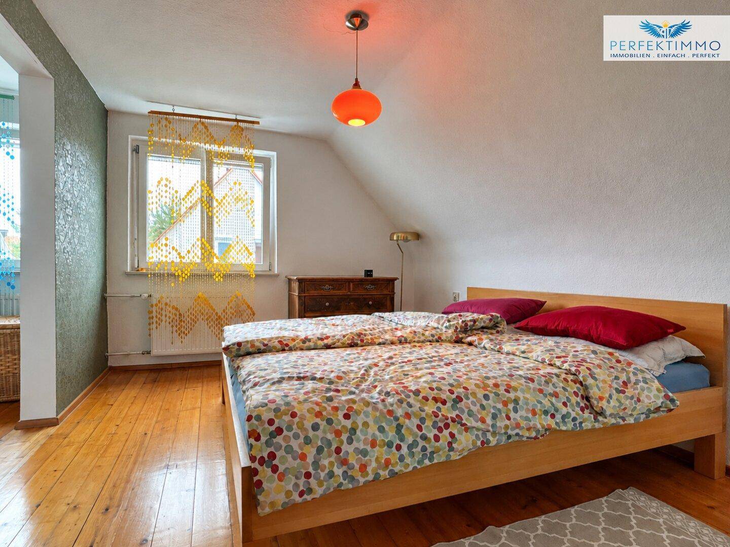 Gemütliches Schlafzimmer im Dachgeschoss mit Holzbett, farbenfroher Bettwäsche und Holzboden.