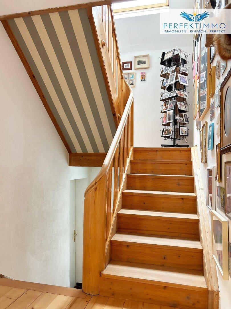 Holztreppe mit Geländer und einer Wanddekoration aus vielen gerahmten Bildern.